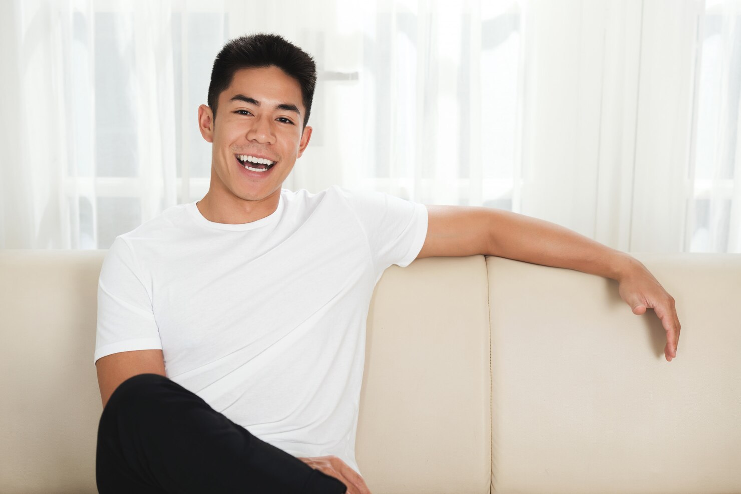 cheerful-young-asian-man-sitting-couch-home_1098-20135
